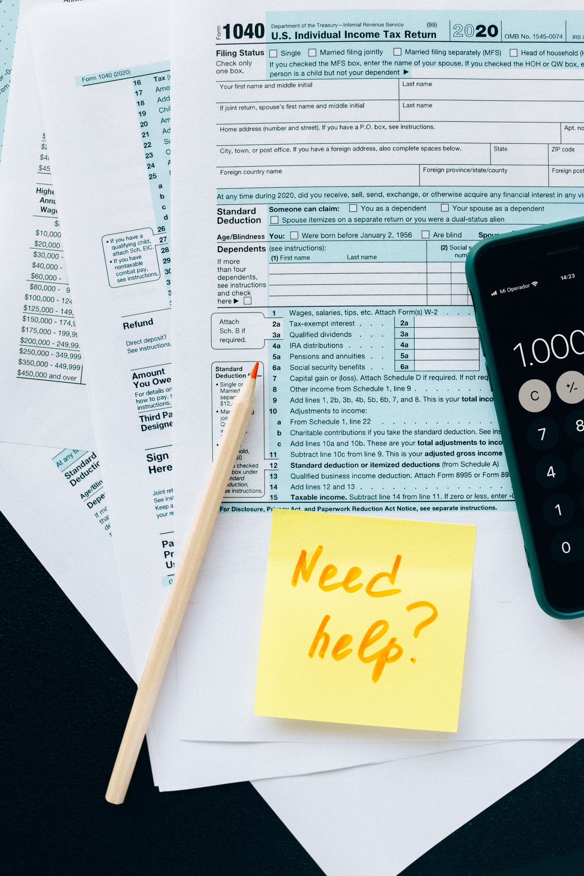 Tax forms with pencil, smartphone, and yellow sticky note reading “Need help?”
