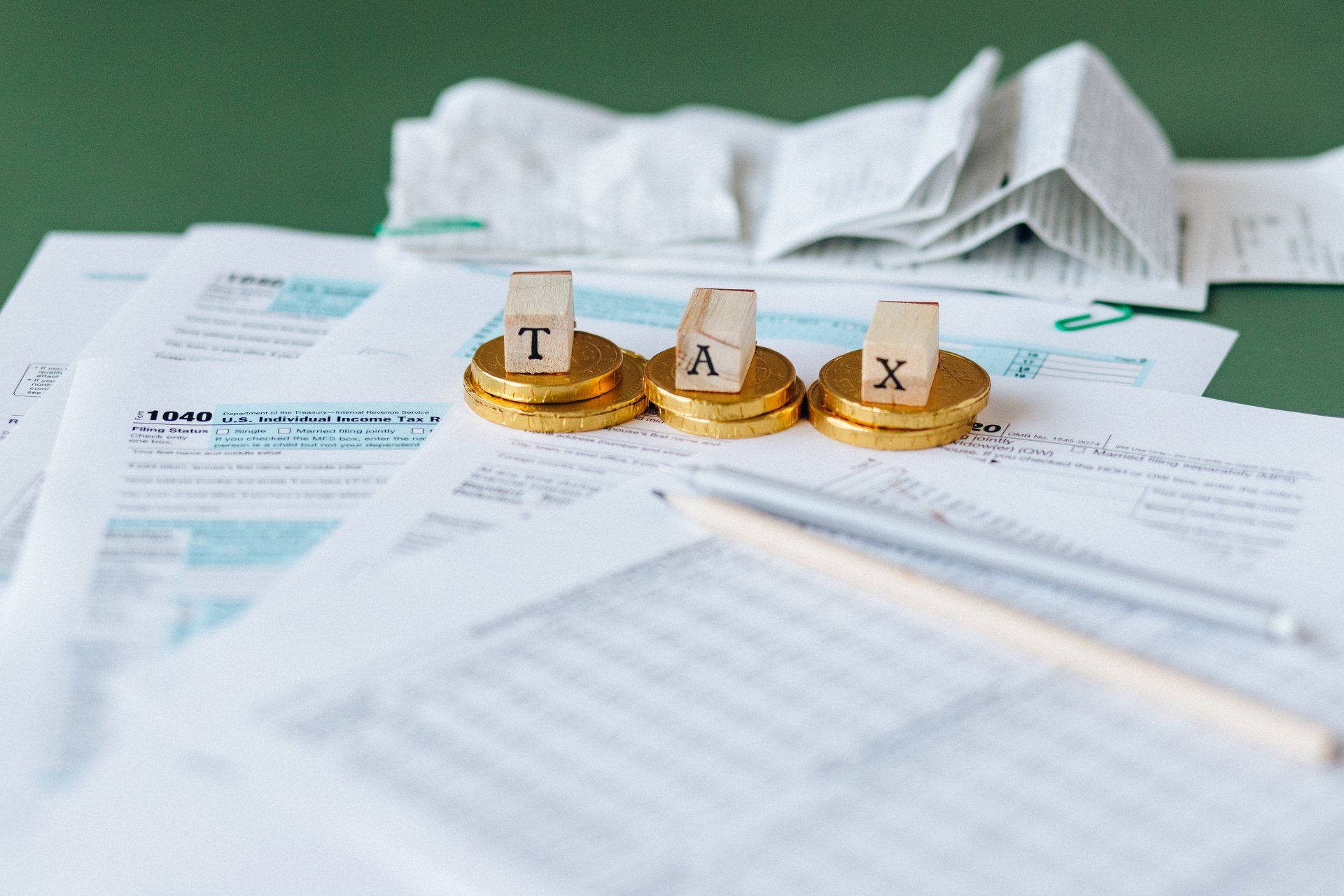 Tax documents with wooden letter blocks spelling TAX on gold coins and a pen in the foreground